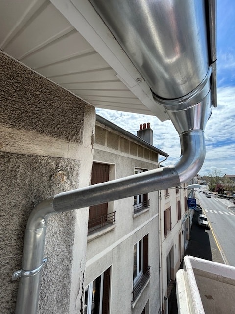Gouttière en zinc et descente : installation de toiture Gouttière en zinc et descente d'eau pluviale installées sur une façade de bâtiment avec vue sur la rue.